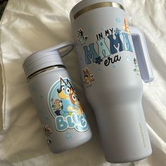 two travel mugs sitting next to each other on a bed