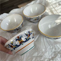 three white bowls with yellow and blue designs on them sitting on a plastic wrapper