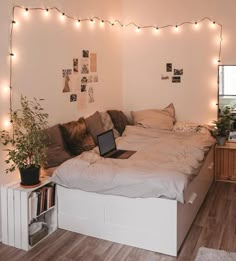 a laptop is sitting on top of a bed with lights strung over the headboard