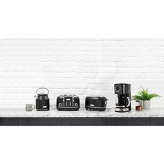 there are many different appliances on the counter in front of a white brick wall with a potted plant next to it