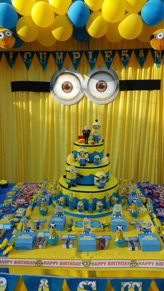 a table topped with a cake covered in blue and yellow frosting next to balloons