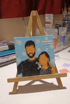 a small easel with a painting of two people on it sitting on a table