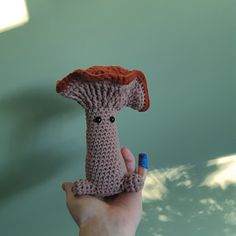 a hand holding a tiny crocheted animal with a red hat on it's head