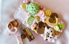 an assortment of candies and cookies on a pink tray next to a cell phone