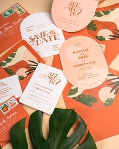 wedding stationery and save the date cards on top of an orange background with tropical leaves