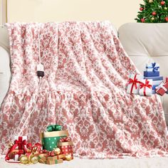 a living room with christmas presents under a pink blanket on the floor and a white couch