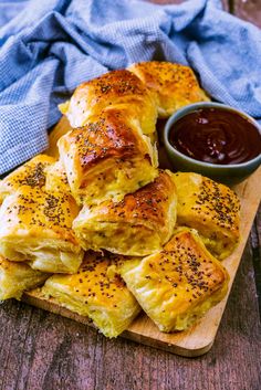 a wooden cutting board topped with cheesy pastries and a bowl of dipping sauce