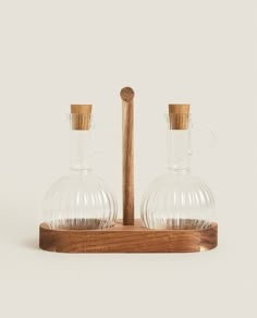 two clear glass carafes with wooden handles on a wood stand against a white background