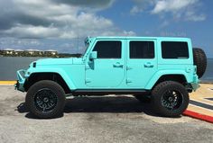 a bright blue jeep is parked in front of the water on a partly cloudy day