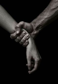 black and white photograph of two people holding each other's hands in the dark