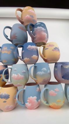 a stack of coffee cups with clouds painted on the outside and inside one is blue, yellow, pink, and white