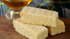 three pieces of cake sitting on top of a wooden cutting board next to a glass of tea