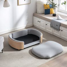 a dog bed in the middle of a living room next to a couch and window