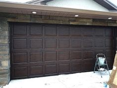 a brown garage door in front of a brick building with a bucket on the ground