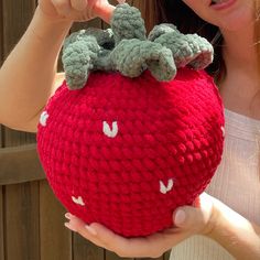 a woman holding up a crocheted red apple with two green leaves on it