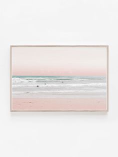 a pink and blue ocean scene with surfers in the water, framed on a white wall