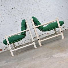 two green chairs sitting next to each other in front of a white brick wall