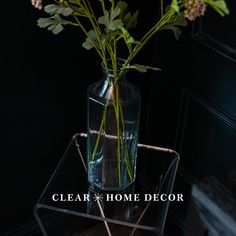 a clear vase filled with flowers sitting on top of a glass table next to a black wall