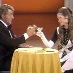 a man and woman sitting at a table toasting with wine glasses