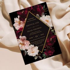 a black and red floral wedding card on a white cloth with gold trimmings