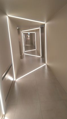 an empty hallway with white walls and light at the end is lit by bright lights