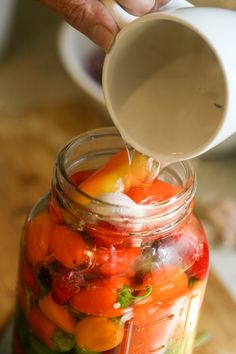 a person pouring water into a jar filled with tomatoes