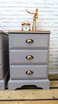 a grey dresser with a clock on top and a small wooden figure next to it