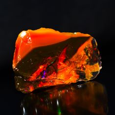 a piece of orange and yellow rock sitting on top of a black surface with reflections