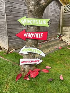 a tree with directional signs on it in front of a wooden fence and building behind it