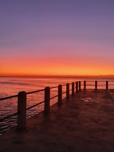 the sun is setting over the water and there are wooden posts in front of it