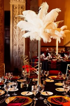 a tall centerpiece with white feathers sits on top of a table set for an event