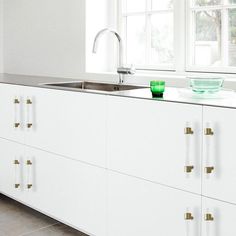 a kitchen with white cabinets and green glassware on the counter top, in front of a window