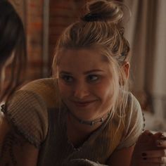 a woman is smiling while sitting next to another woman in a room with brick walls