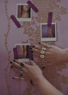 two hands with rings and nail polish holding pictures on the wall behind them, while another person holds up their nails