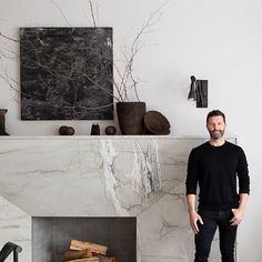 a man standing next to a fireplace in a living room with white walls and black furniture