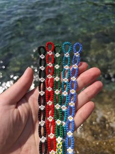 a hand holding four different colored bracelets in front of the ocean and rocks on the shore