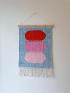 Introduce a calming yet vibrant element to your space with this handwoven tapestry, Soft Glow. This abstract wall hanging features three layered shapes in warm red and soft pinks, set against a serene blue backdrop. The gentle gradient of colours creates a harmonious and modern look, complemented by a soft cream fringe that adds texture and elegance. Crafted using traditional weaving techniques, this small fibre art piece is perfect for bringing a minimalist, contemporary touch to your decor. Whether displayed in a living room, bedroom, or nursery, it offers a splash of colour and artistic flair. Dimensions: 8 inch x 12 inch Materials: Wool, cotton, wooden dowel Handwoven in South London Ready to hang with a natural wooden dowel and cotton string Ideal for Scandinavian, contemporary, or mi Handwoven Tapestry, Blue Backdrops, Fibre Art, Minimalist Contemporary, Warm Red, Traditional Weaving, Cotton String, South London, Small Wall