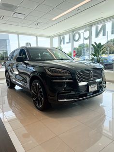 a black suv is parked in a showroom with large windows and white tile flooring