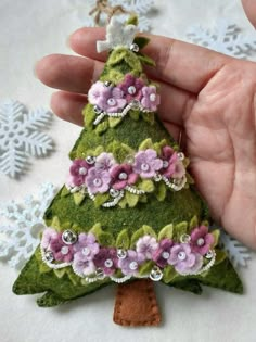 a hand holding a small green christmas tree ornament with pink and purple flowers