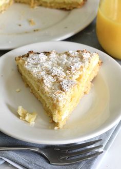 a slice of cake on a plate with a fork and glass of orange juice in the background