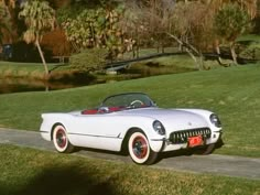 an old white convertible car parked on the side of a road in front of some trees