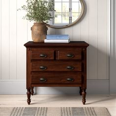 a wooden dresser sitting in front of a mirror on top of a white wall next to a rug