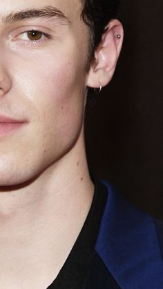 a close up of a young man wearing a blue jacket and black shirt with ear piercings