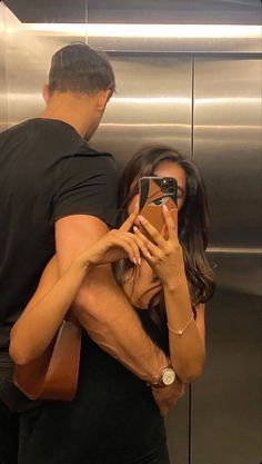 a man standing next to a woman in front of an elevator holding a cell phone