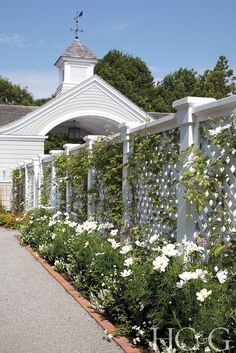 a white building with flowers growing on the side of it and a walkway leading to it