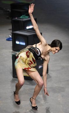 a woman standing on top of a stage holding her hand up in the air while wearing high heels