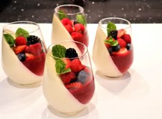 four glasses filled with fruit and mint garnish on top of a white table