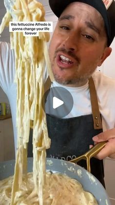 a man in an apron is holding a ladle full of spaghetti and looking at the camera