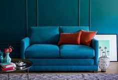 a living room with teal walls and a blue couch in the corner, surrounded by books