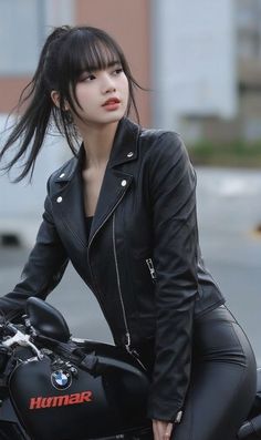 a young woman sitting on top of a motorcycle wearing black leather pants and a jacket